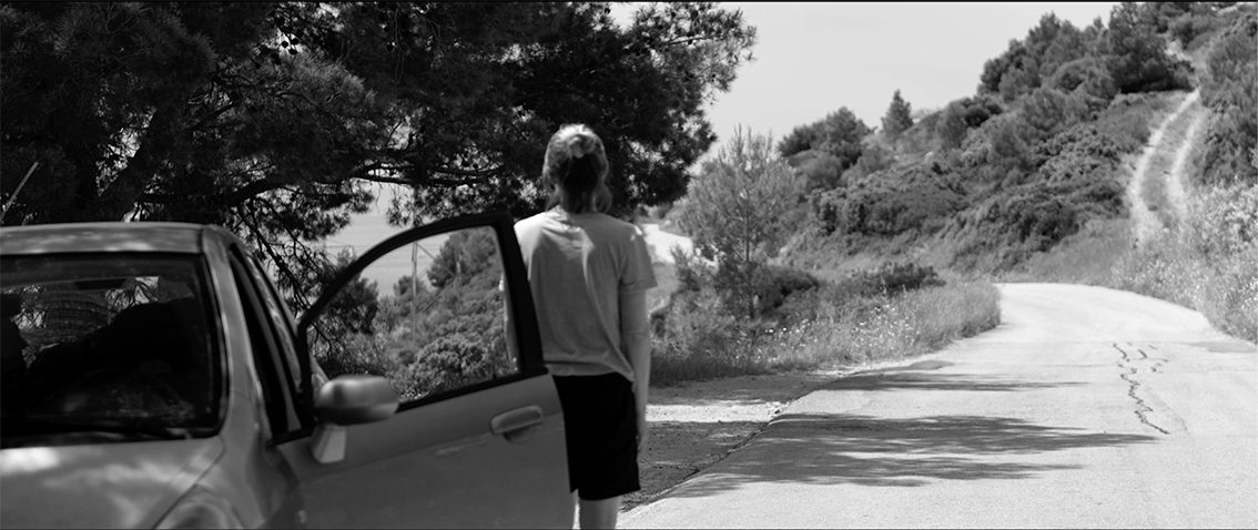 Frau steht vor einem Auto und blickt in die Ferne.