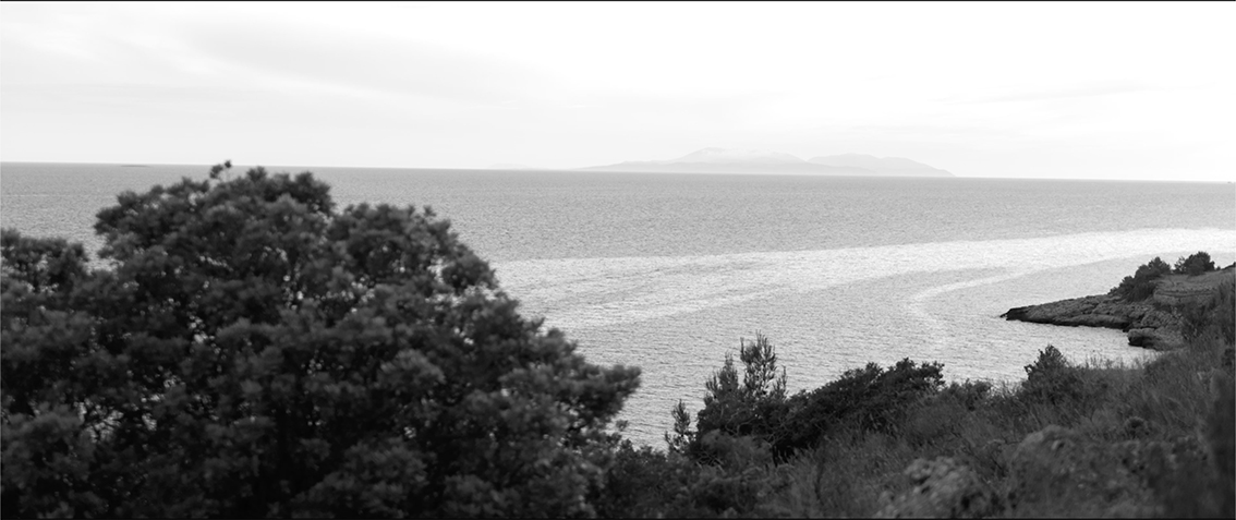Meer mit Kielwasser. In der Ferne eine Insel.